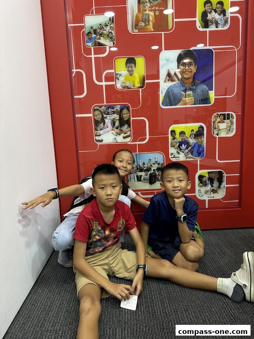 Three young boys posing in front of a wall decorated with photos of children.