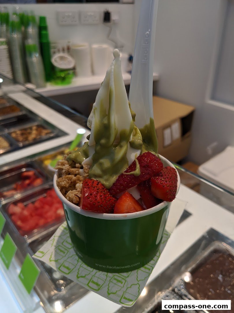 A cup of frozen yogurt with strawberries and granola, topped with green sauce.
