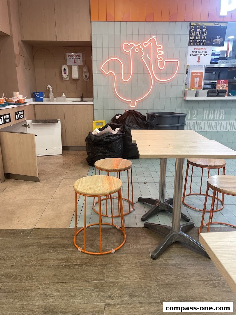 Interior of a Popeyes restaurant with seating, a counter, and a neon chicken sign.