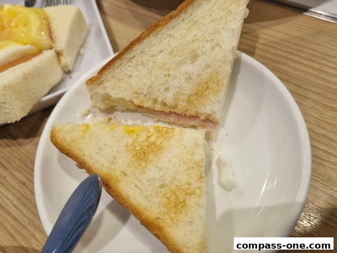 Close-up of a toasted sandwich with ham and a dollop of sauce on a white plate.