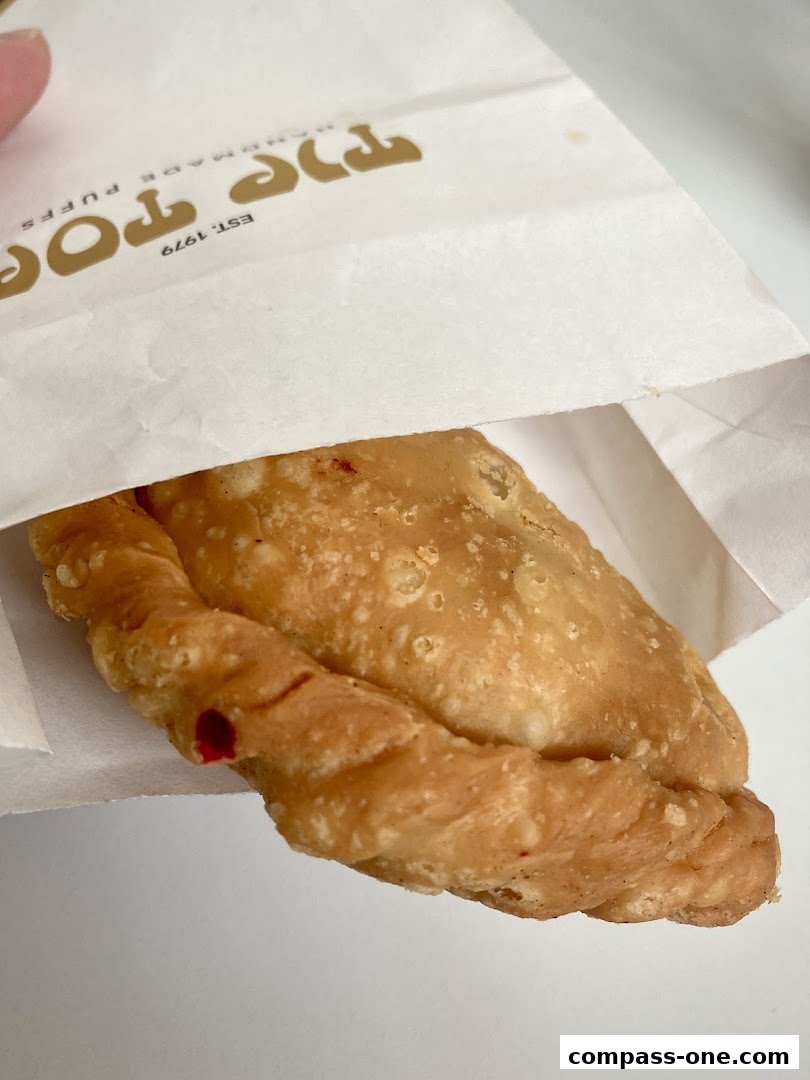 A close-up of a golden-brown curry puff peeking out of a branded paper bag.