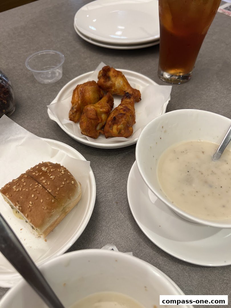 A table setting with chicken wings, a sandwich, soup, and a drink.