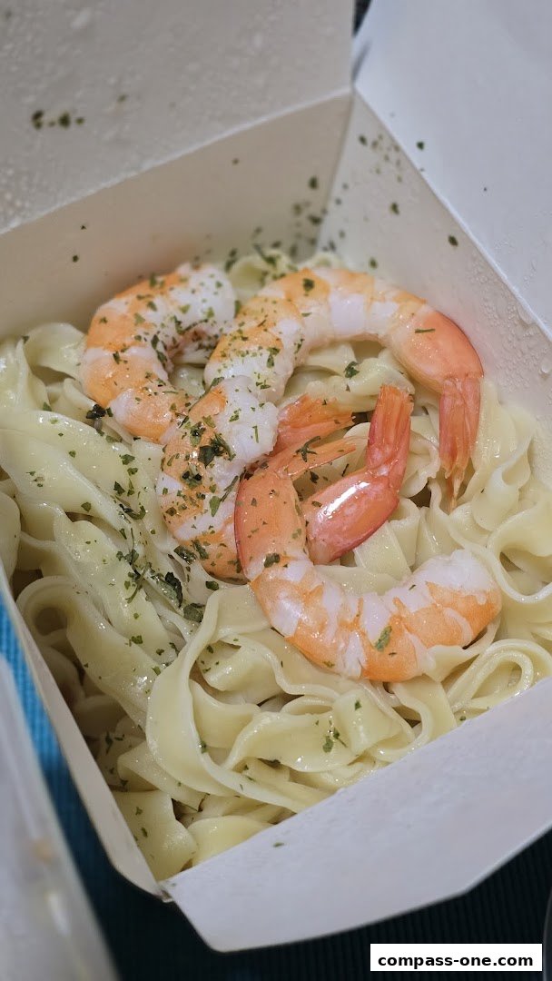 A close-up of fresh pasta with succulent shrimp and sprinkled herbs in a takeaway box.