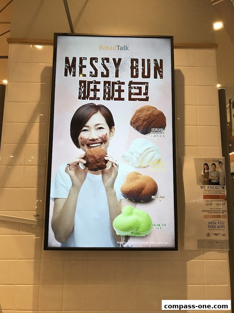 A woman happily holding a messy bun with various flavored buns displayed around her.