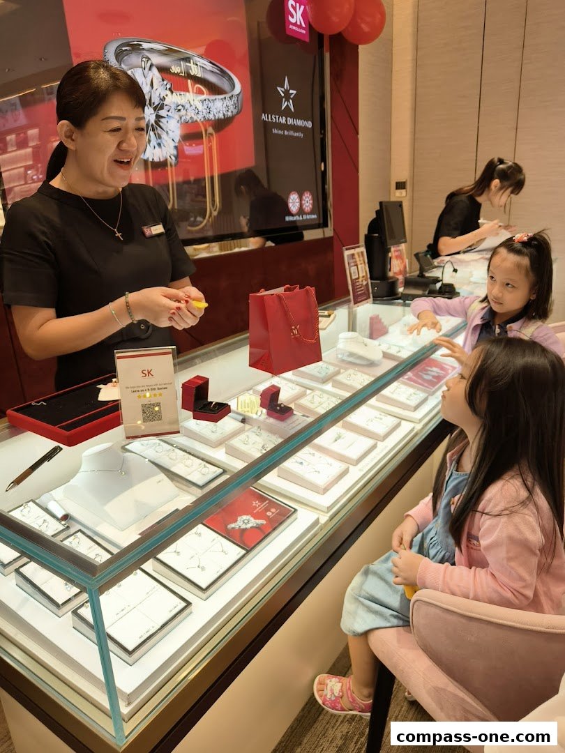 A jeweler assists two young girls at a display case filled with jewelry.