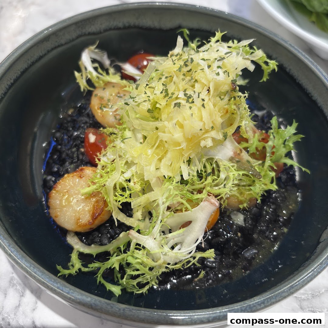 A close-up of a gourmet dish featuring seared scallops on black risotto with fresh greens.
