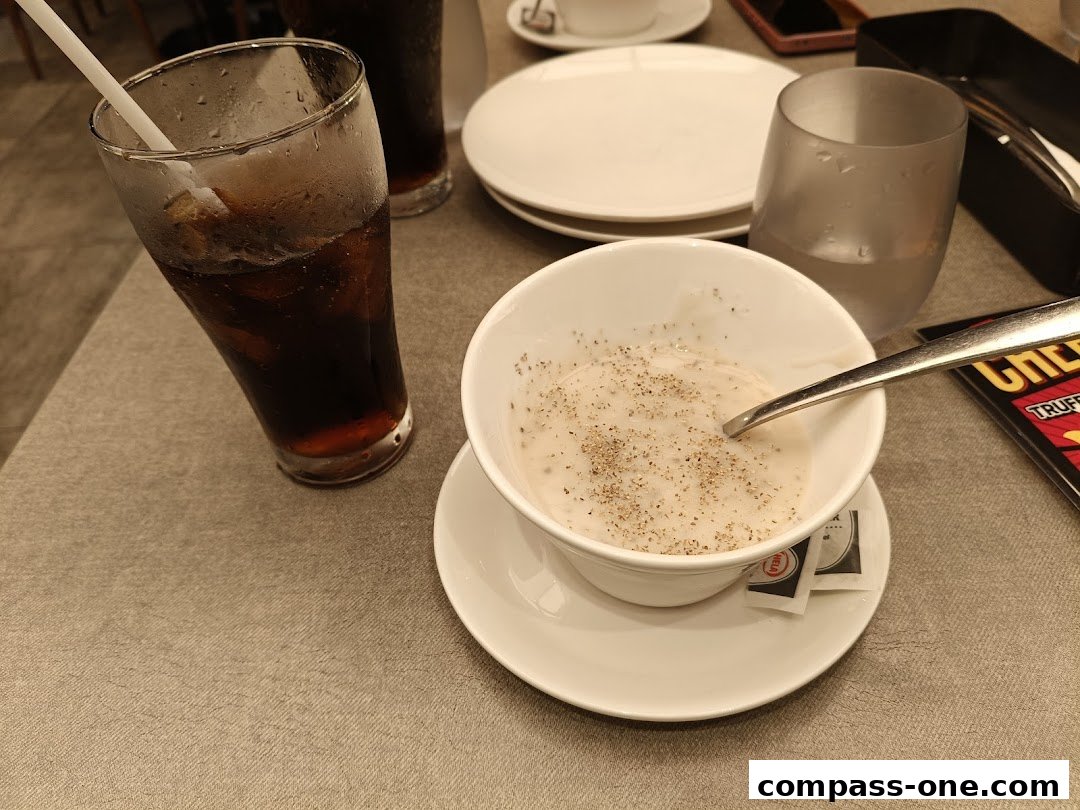 A close-up of a bowl of soup with a spoon, a glass of cola, and plates on a table.
