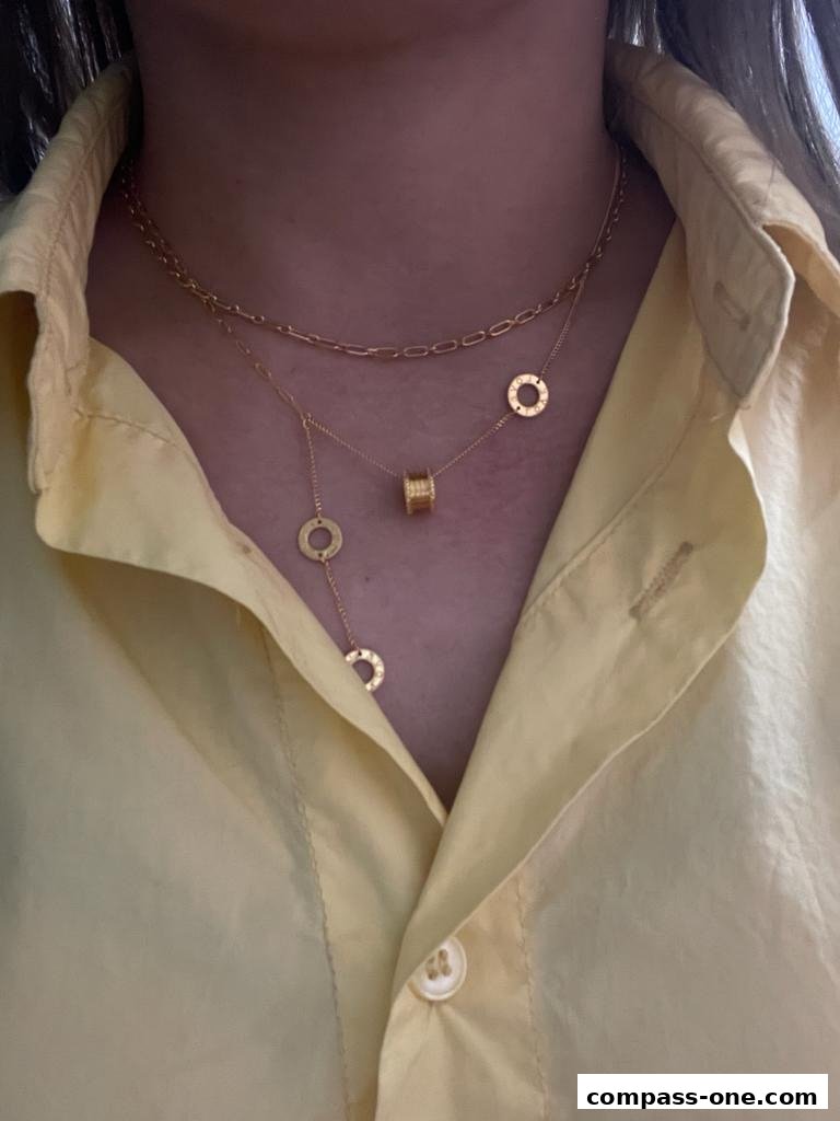 A person wearing a yellow shirt and layered gold necklaces with circular pendants.
