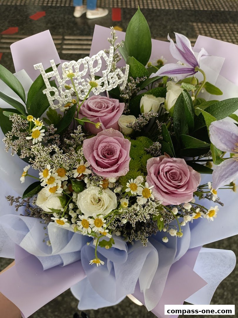 A beautiful bouquet of pink roses, white roses, and daisies with a 'Happy Birthday' topper.