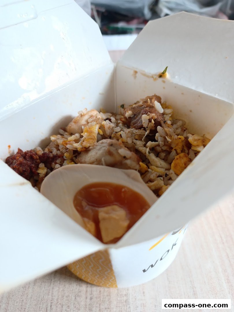A close-up of a takeaway box filled with fried rice, chicken, and a hard-boiled egg with sauce.