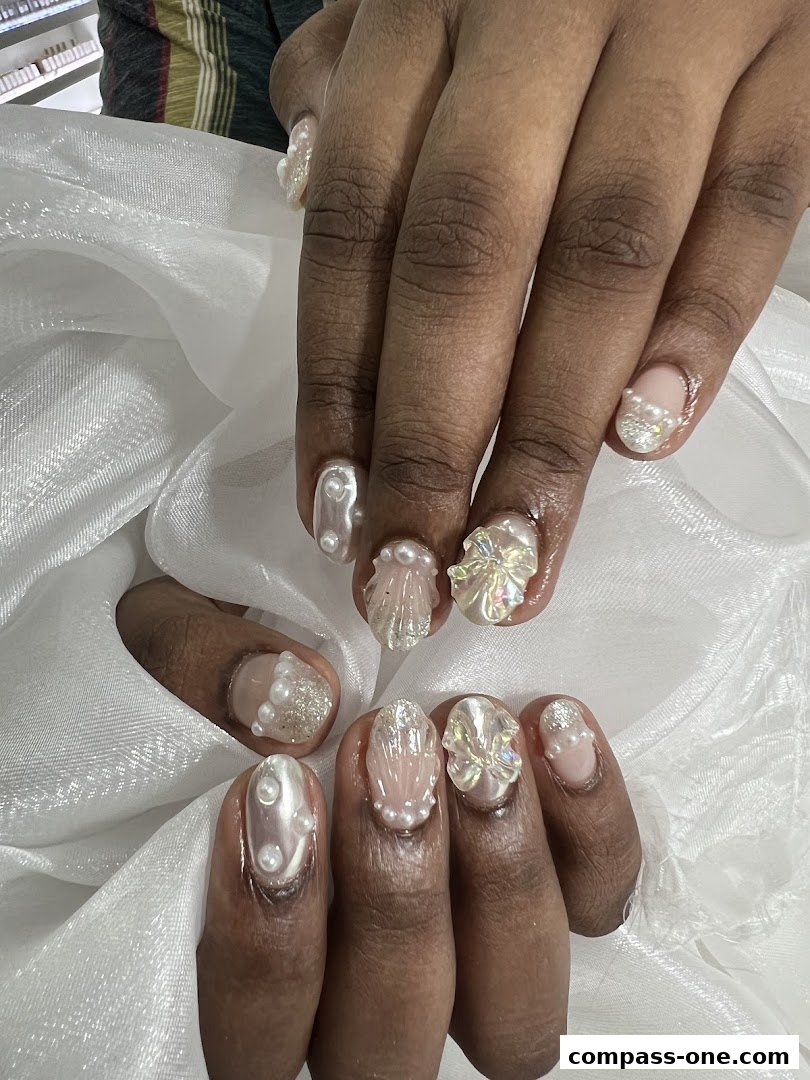 Close-up of hands with elaborately decorated nails featuring pearls and iridescent embellishments.