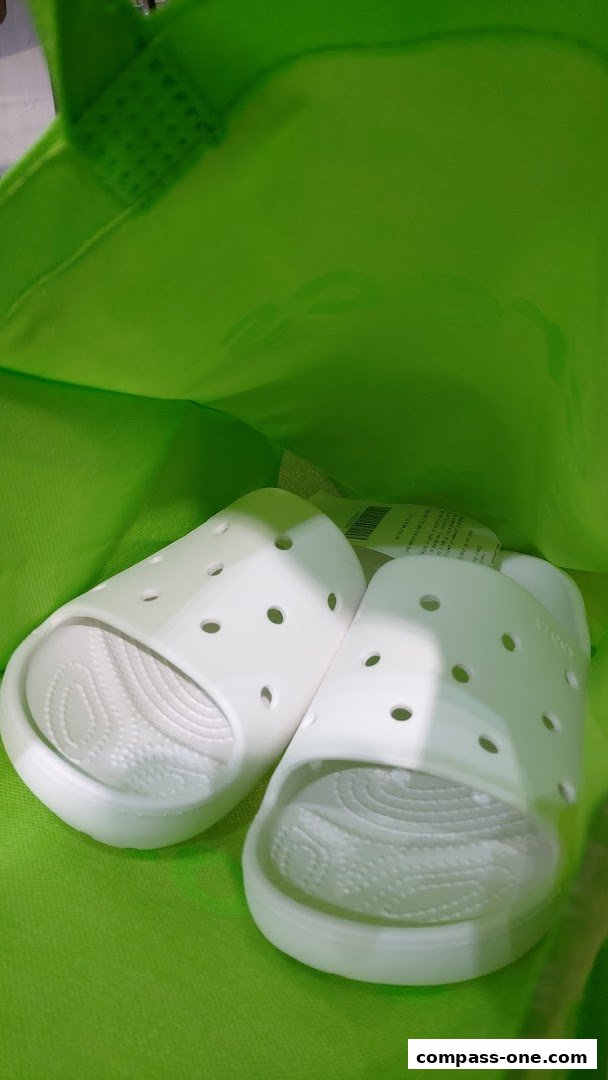 A pair of white Crocs slides inside a bright green shopping bag.