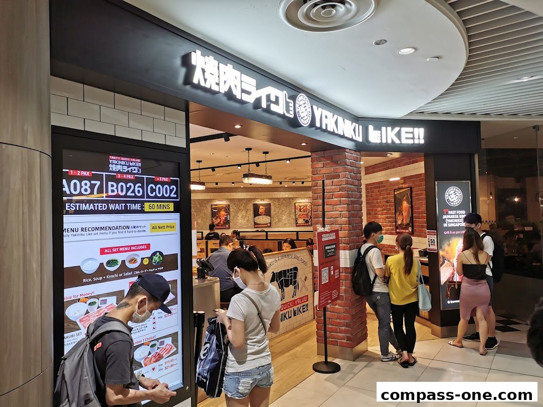 People waiting outside Yakiniku Like, a Japanese BBQ restaurant, with a digital queue display.