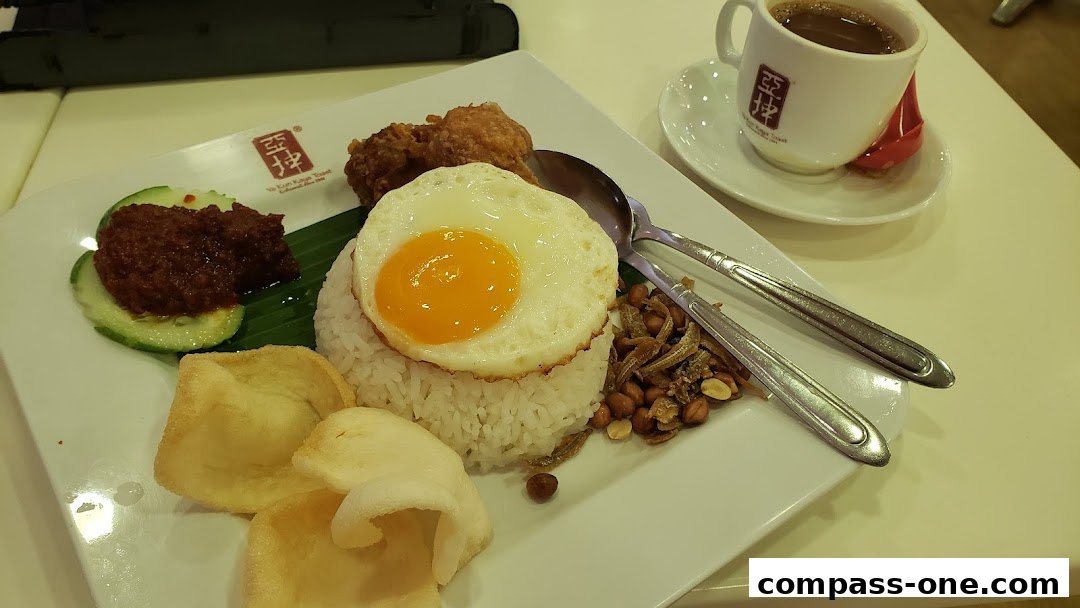 A plate of Nasi Lemak with fried chicken, sunny-side-up egg, and a cup of coffee.