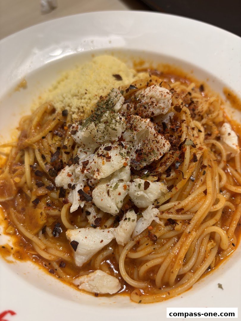 A close-up shot of a delicious crab pasta dish with shredded cheese and chili flakes.