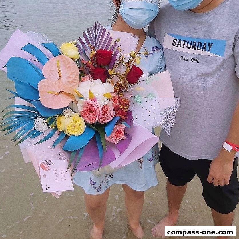 A couple holding a vibrant bouquet of flowers on a beach.