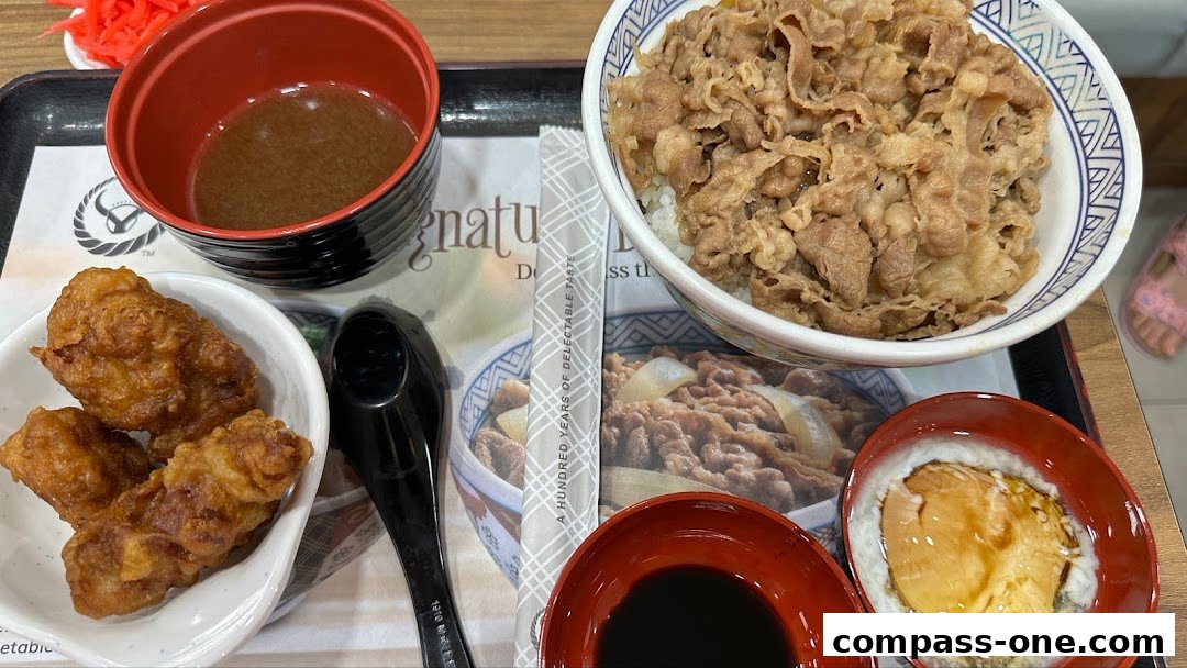 A tray of Yoshinoya food including beef bowl, fried chicken, soup, and a side dish.