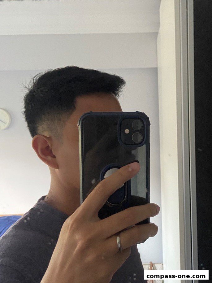 A person is taking a mirror selfie, showcasing a fresh haircut and a phone.