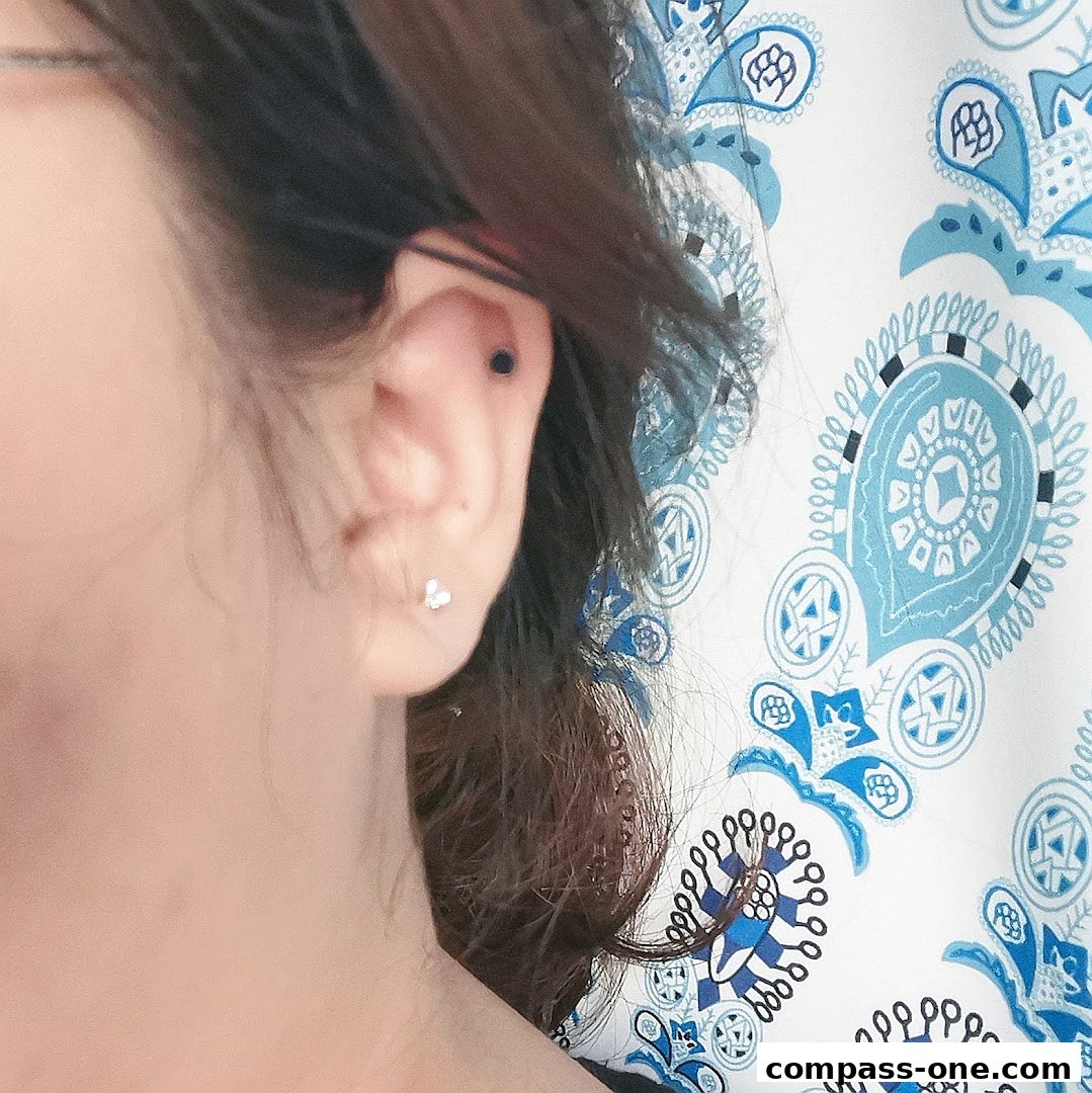 Close-up of a person's ear with two small earrings, against a patterned background.