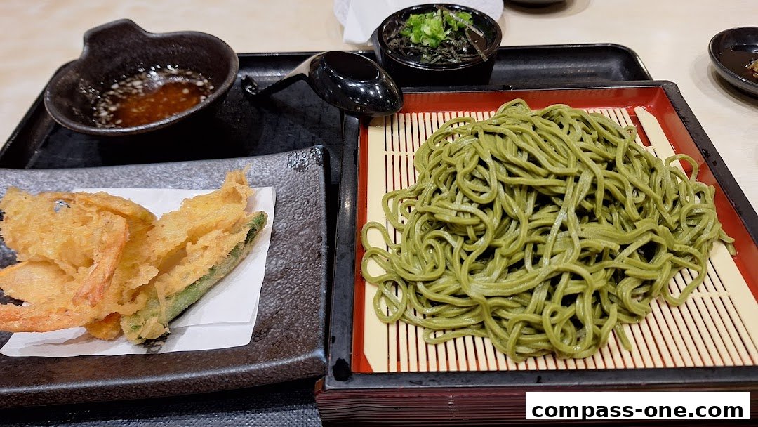 A plate of green soba noodles with tempura and dipping sauce.