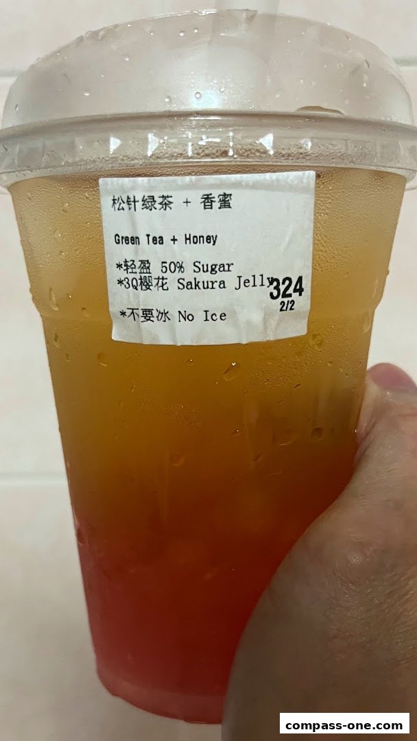 A hand holds a refreshing Green Tea + Honey beverage with Sakura Jelly and 50% sugar.