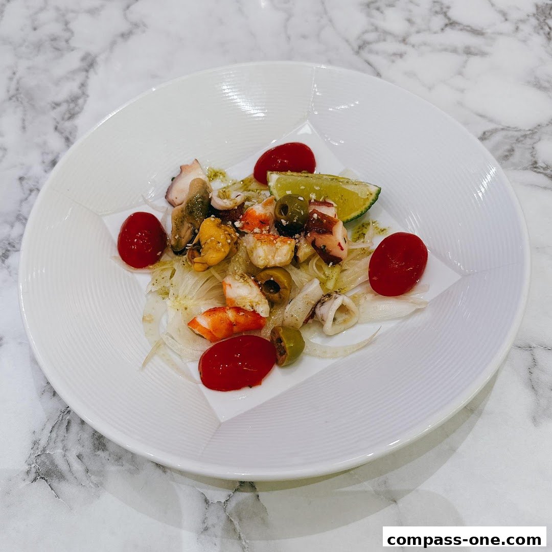A white plate with a seafood salad featuring octopus, shrimp, mussels, calamari, olives, and tomatoes.