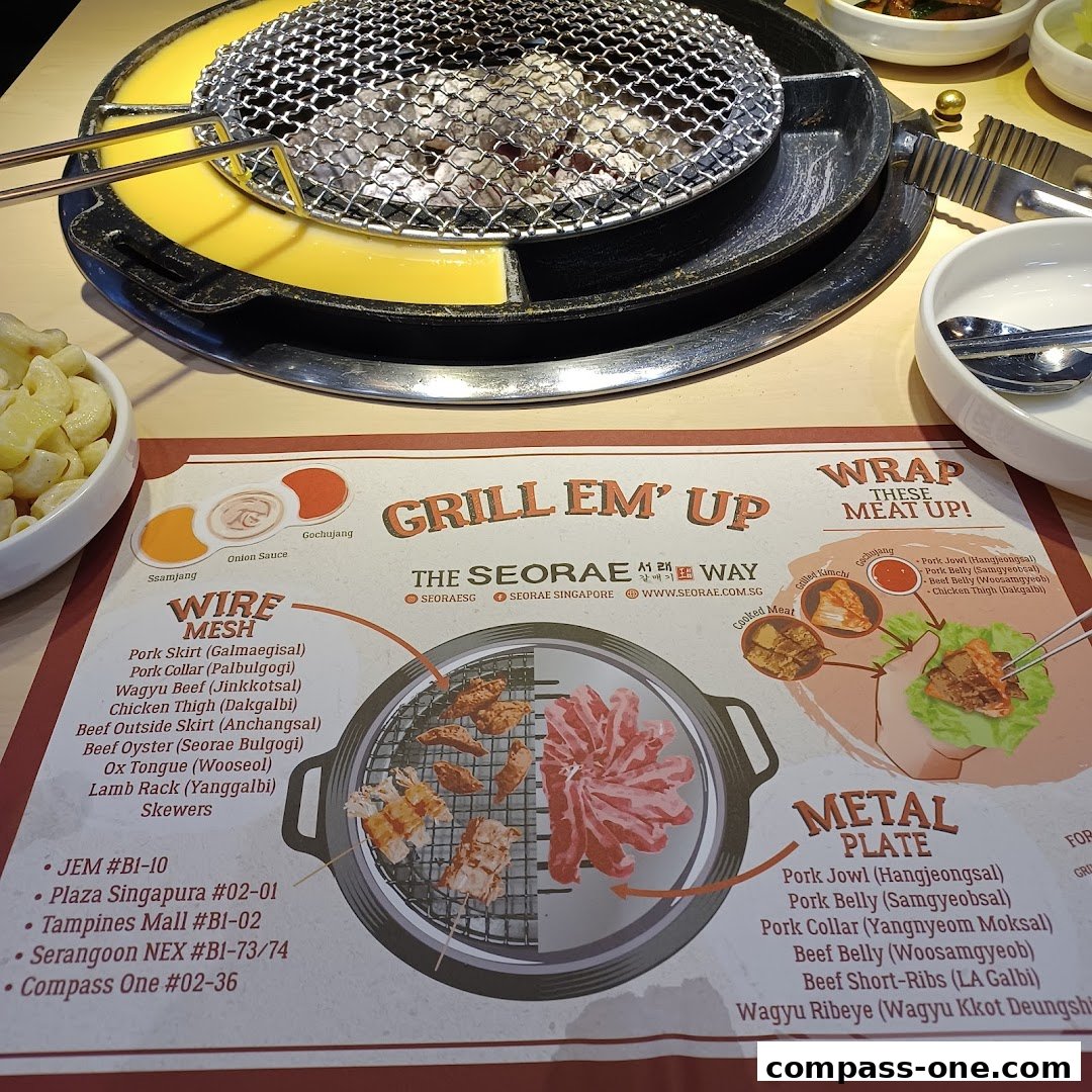 A table setting at a Korean BBQ restaurant with a grill and a menu showing various meat options.