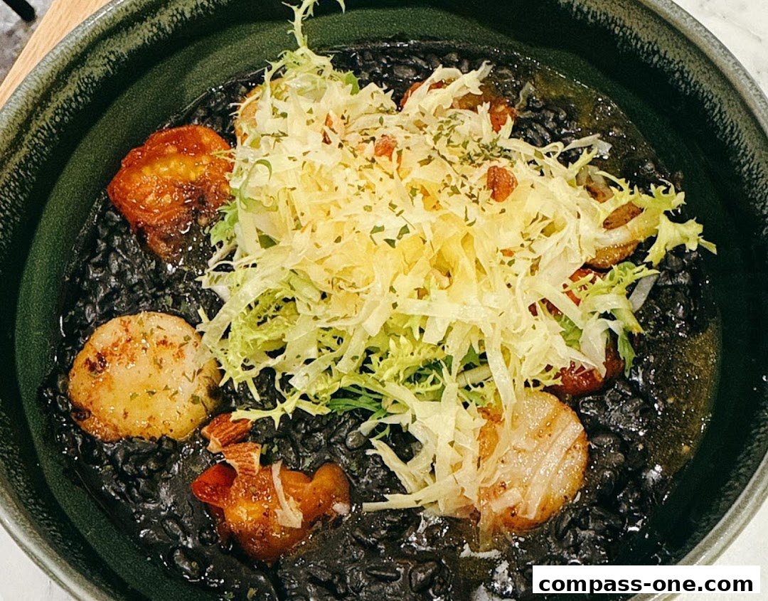 A close-up of a black risotto dish with seared scallops and a fresh salad topping.