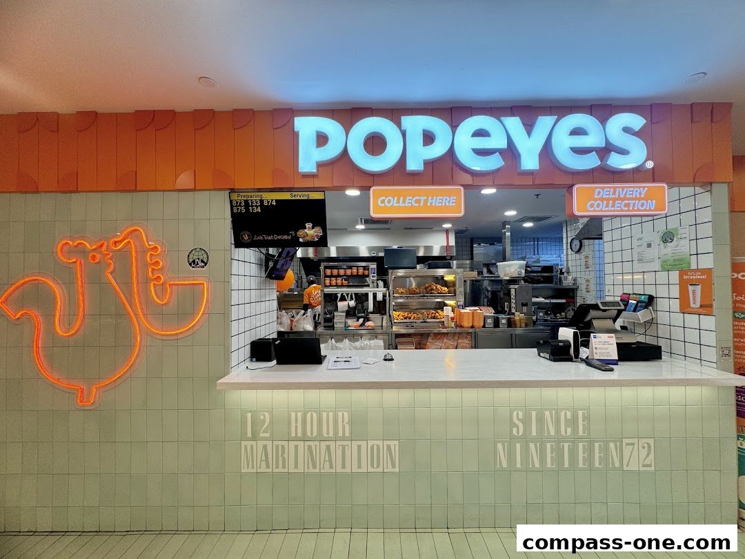 The Popeyes restaurant counter with neon chicken art and the Popeyes logo above.