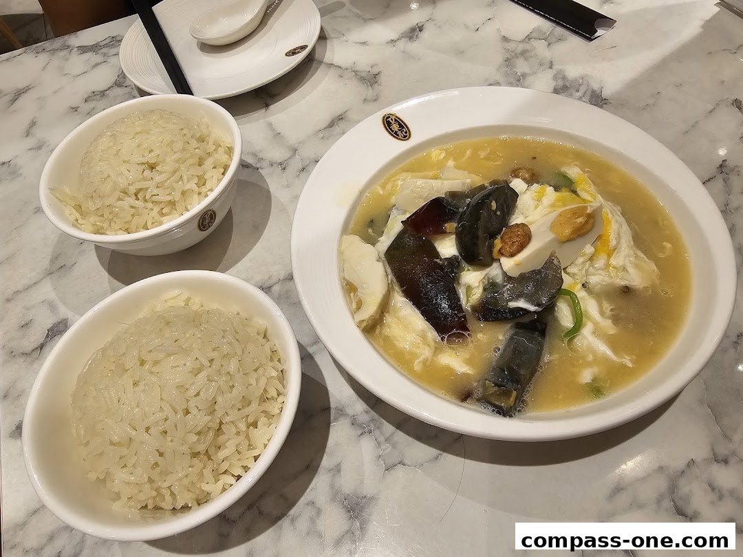 A close-up of a delicious dish with rice and a savory soup with eggs and preserved eggs.