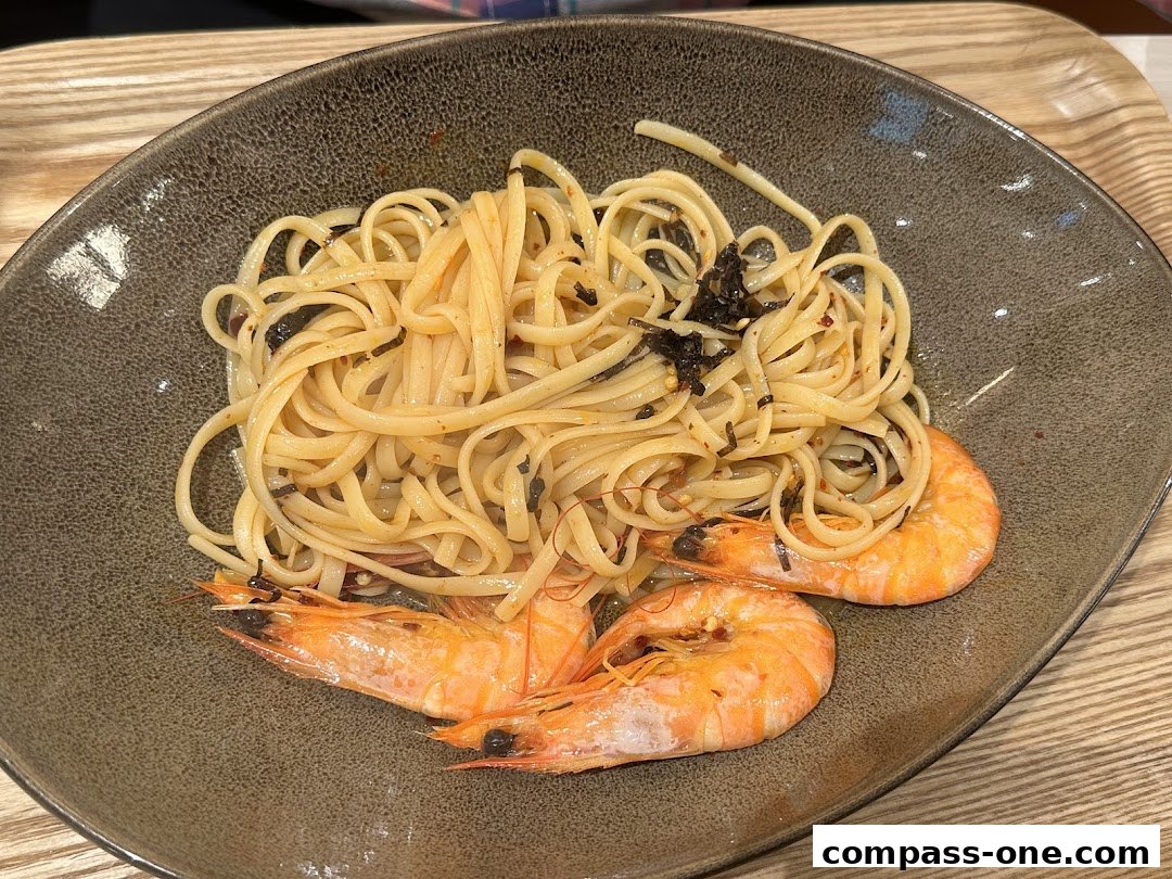 A close-up shot of linguine pasta with three large prawns in a rustic bowl.