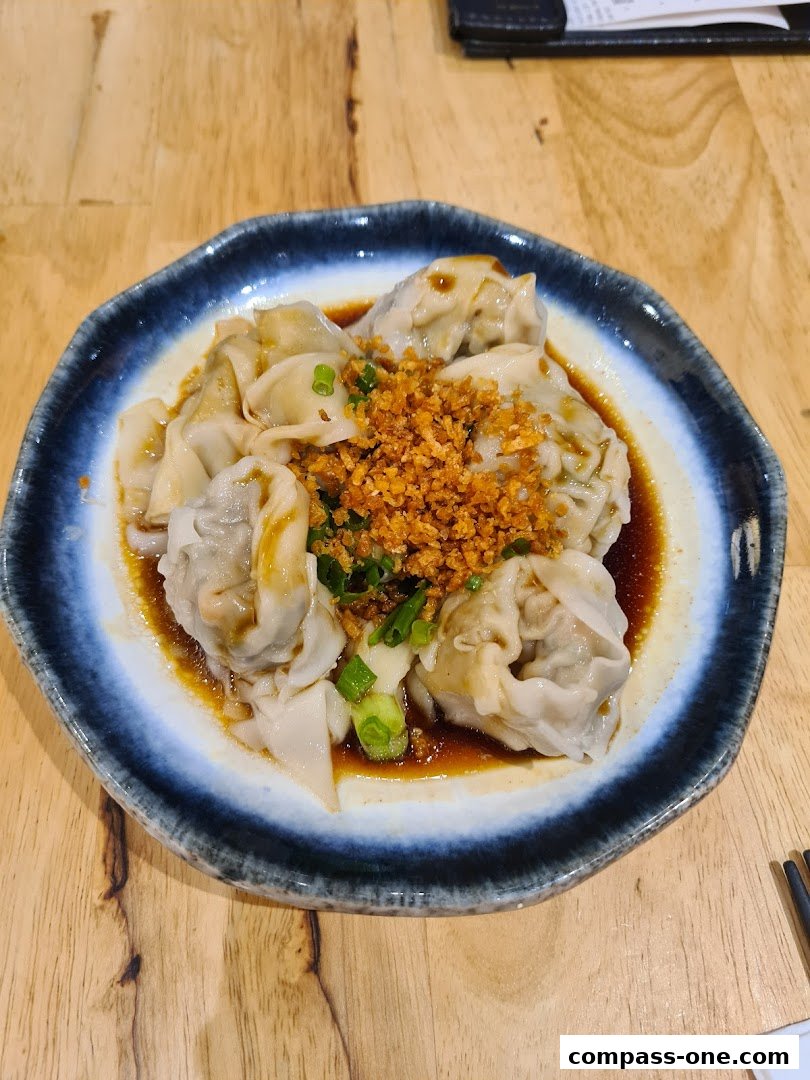 A plate of delicious wontons with sauce, topped with crispy garlic and spring onions.
