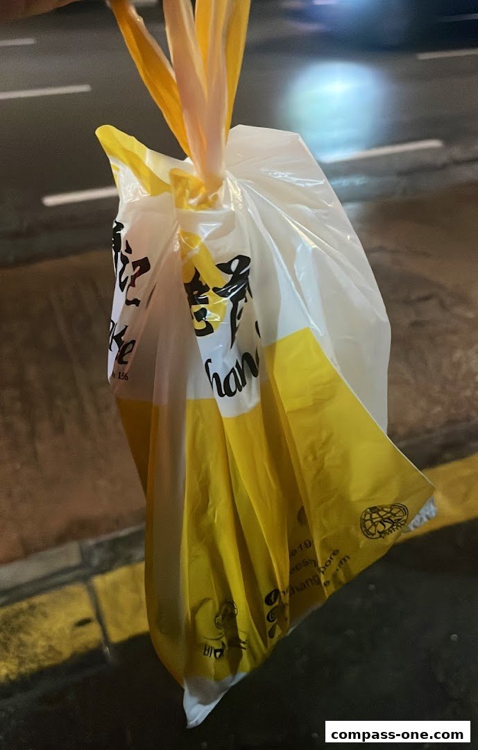 A white and yellow plastic bag from Old Chang Kee, held by its handles.
