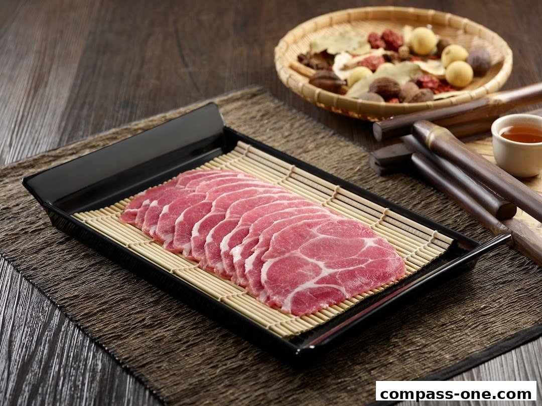 A platter of thinly sliced raw meat arranged on a bamboo mat, with ingredients and tea in the background.