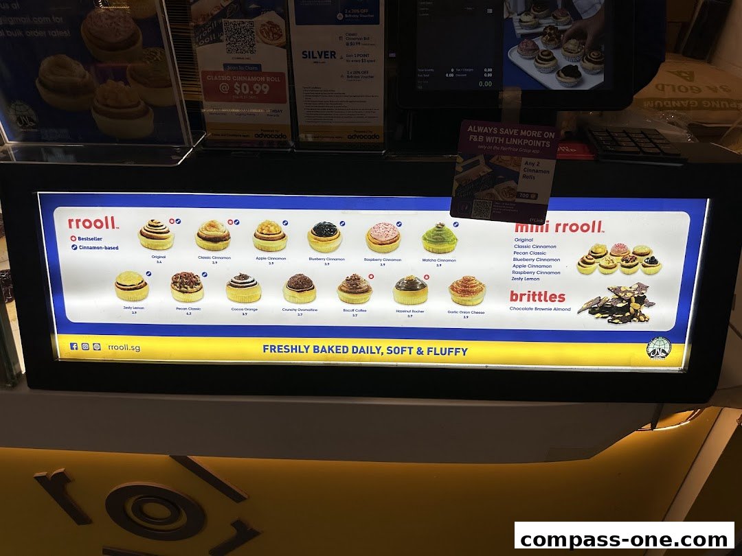 A brightly lit menu board showcasing various cinnamon rolls and brittles offered by rrooll.