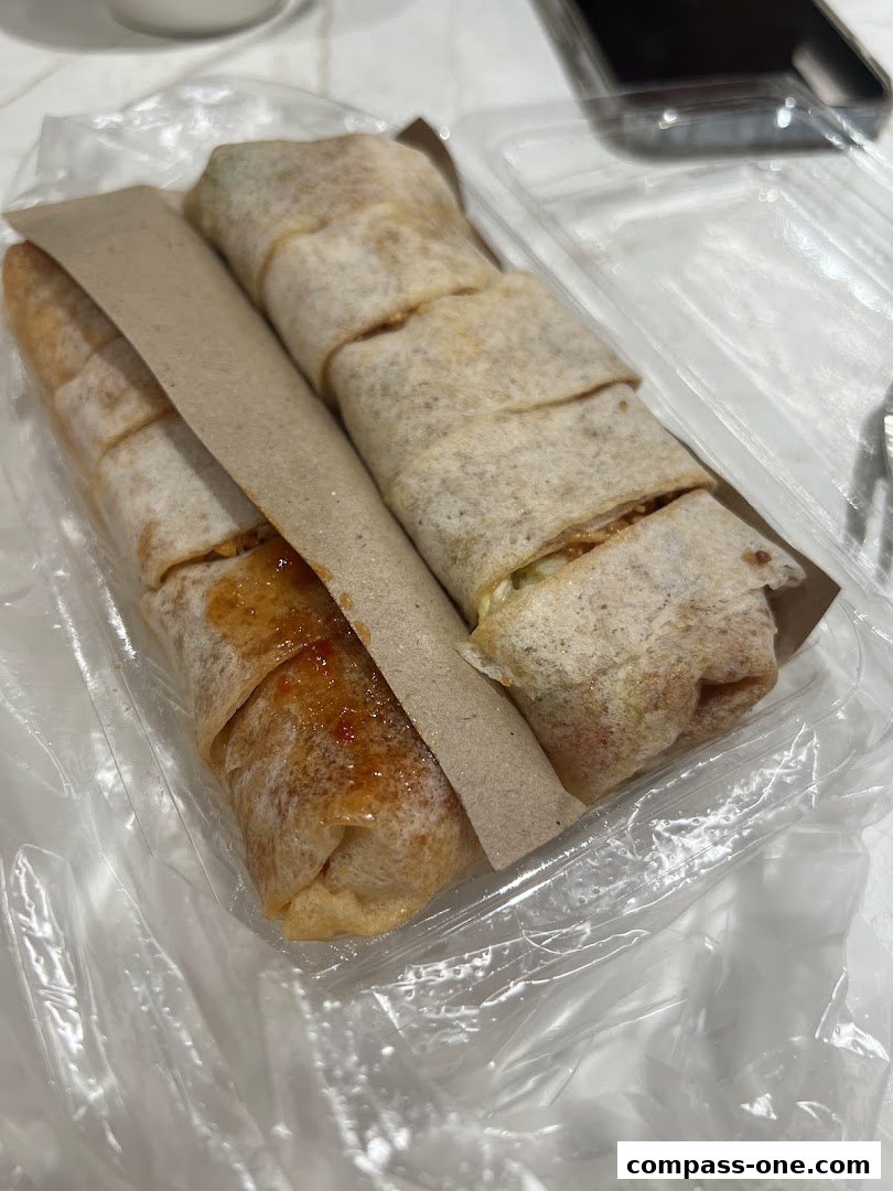Two popiah rolls in a takeaway container, one with a sweet chili sauce.