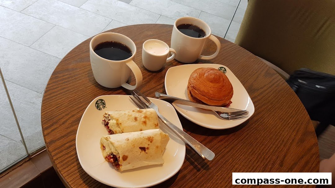 Two wraps, a pastry, and coffee cups are arranged on a wooden table.
