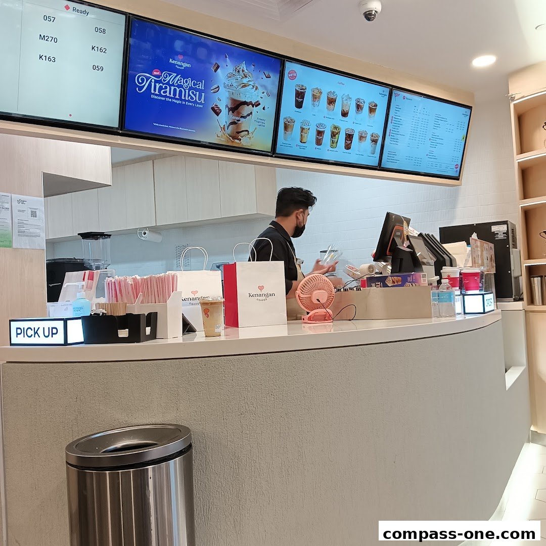 A barista prepares drinks behind a counter at Kenangan Coffee, with digital menus displaying drinks and promotions.