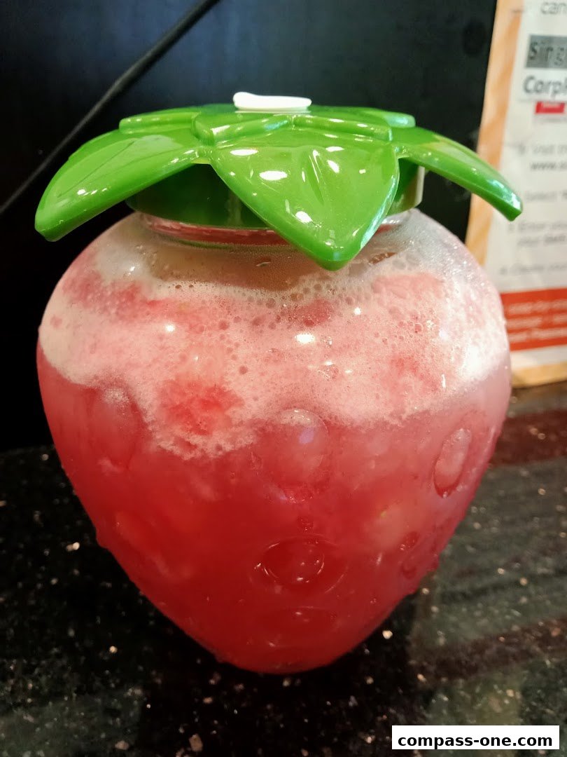 A refreshing pink beverage served in a novelty strawberry-shaped glass with a green leaf lid.