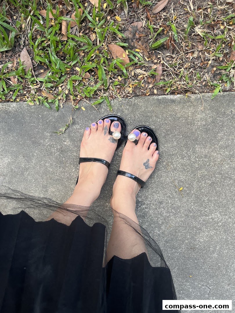 A person's feet wearing black sandals with pearl embellishments and purple nail polish.