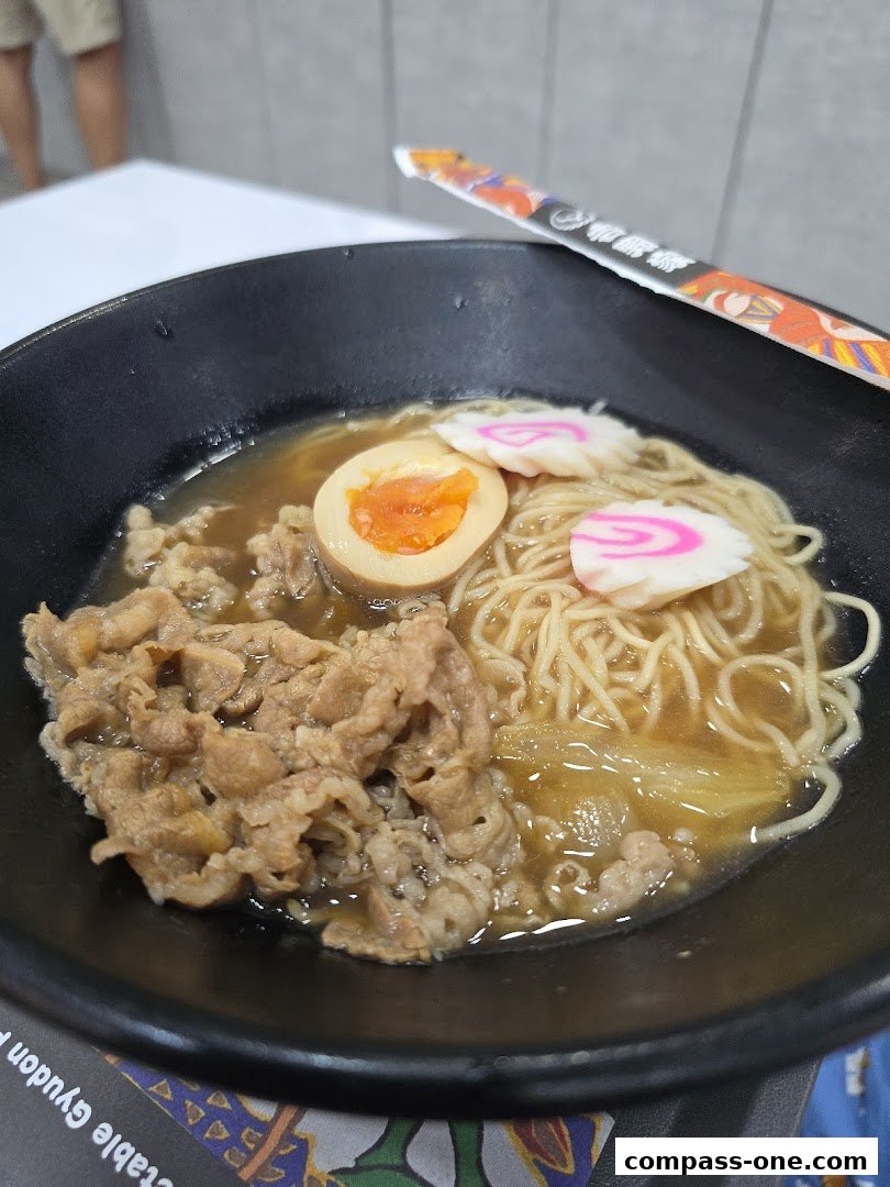 A close-up of a bowl of Yoshinoya's beef ramen with a soft-boiled egg and fish cakes.