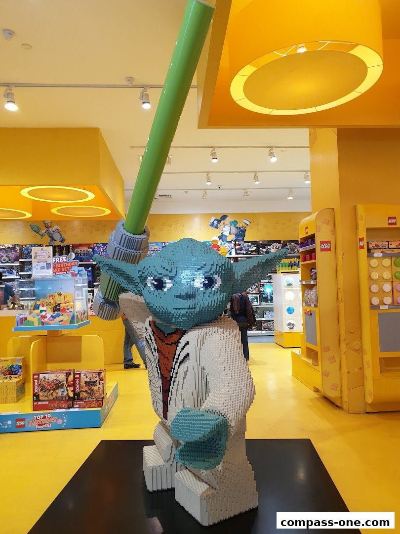 A large LEGO Yoda statue holding a green lightsaber inside a brightly lit store.