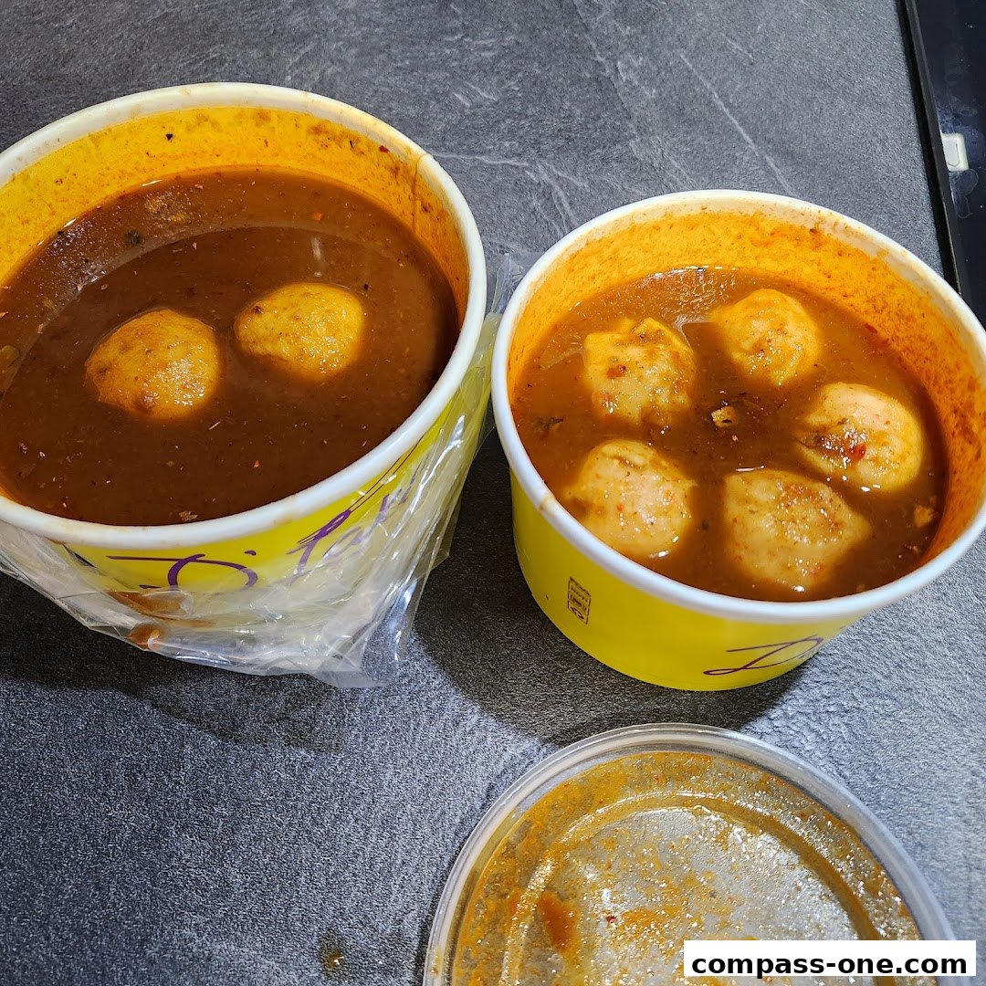 Two takeaway bowls of Laksa with fish balls and a lid with sauce residue.