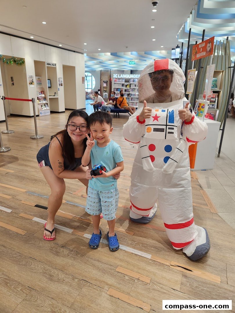 A woman and child pose with a person in an inflatable astronaut costume at Sengkang Public Library.