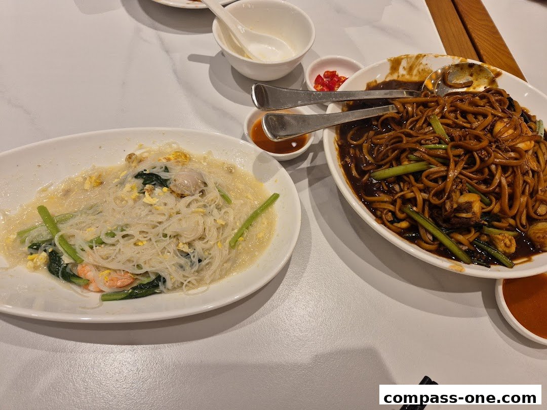 Two plates of noodles and a bowl of chili are on a white table.
