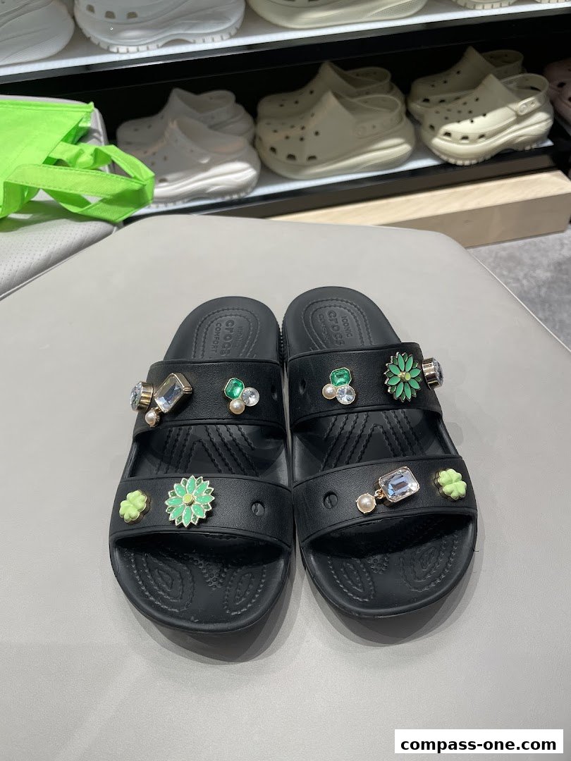 Black Crocs sandals adorned with decorative charms, including flowers and gems.