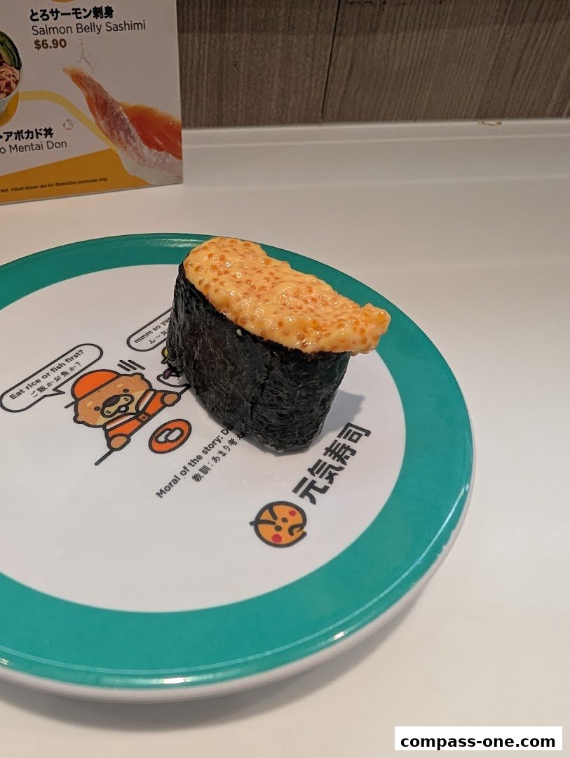 A piece of sushi with creamy orange topping on a decorative plate with Japanese text.