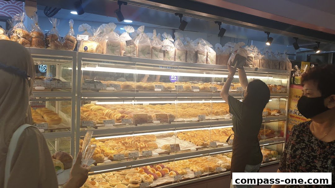 A bakery display case filled with various fresh breads and pastries, with customers browsing.
