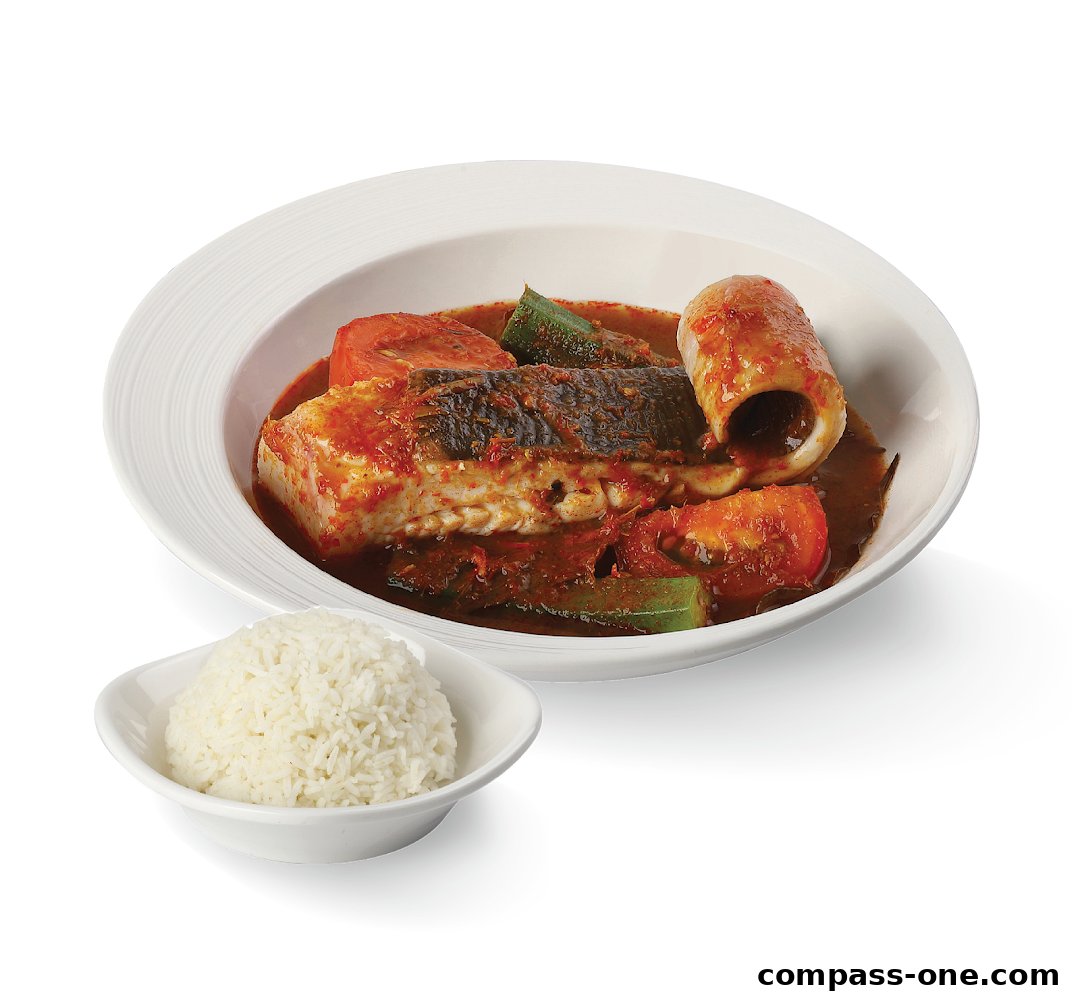 A bowl of fish and squid curry with tomatoes and okra, served with a side of white rice.