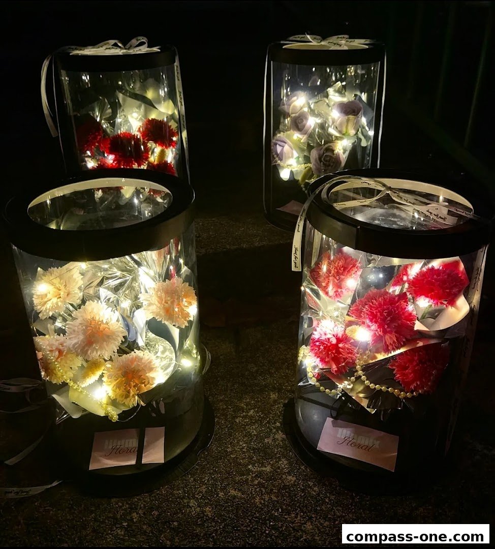 Four illuminated floral arrangements in clear cylindrical containers with ribbons.